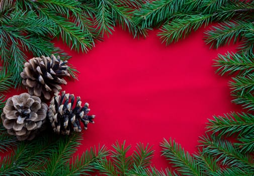 A frame of green fir branches and three cones on a red background. The concept of Christmas and New year. Space for your text.