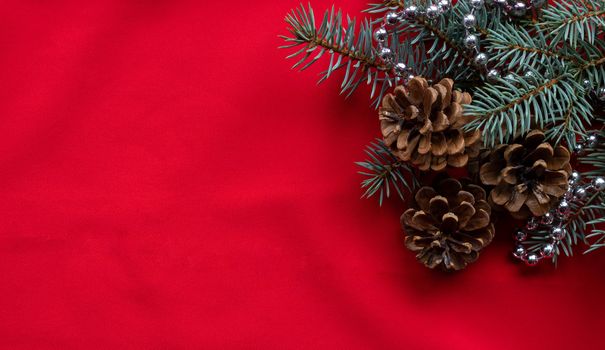 Three pine cones and blue spruce branches with silver beads lie on a red background. The concept of the New year and Christmas.