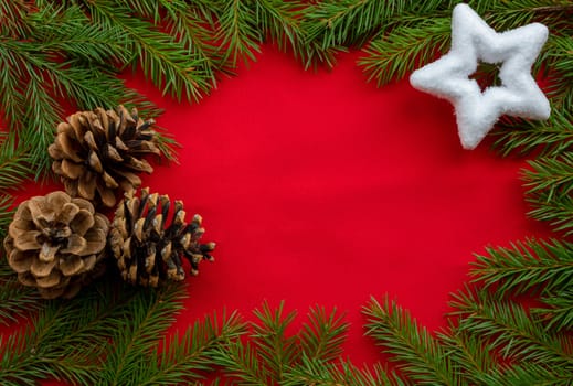 A frame of green fir branches, a white star and three cones on a red background. The concept of Christmas and New year. Space for your text.