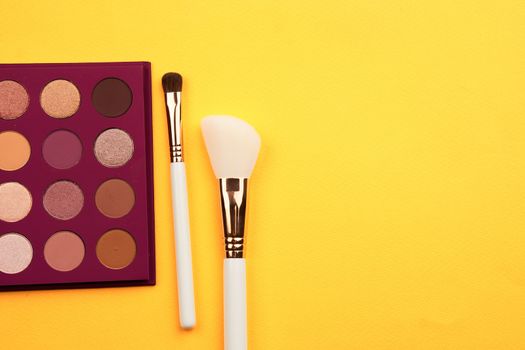 Eyeshadows and makeup brushes on a yellow background top view professional cosmetics. High quality photo