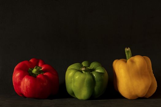 close-up of three bell peppers. red, green and yellow on a dark background