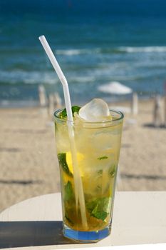mojito cocktail in a glass glass with a straw on the background of the sea beach on a sunny day.