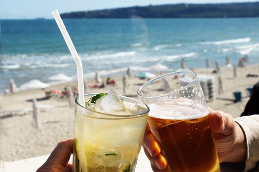 glass with mojito and glass with beer clink glasses on the background of the sea beach.