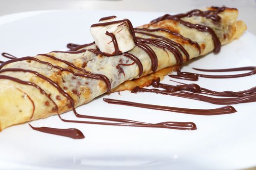 pancake with banana, doused with chocolate on a plate close up