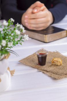 Young woman praying and Taking communion  - the wine and the bread symbols of Jesus Christ blood and body with Holy Bible. Easter Passover and Lord Supper concept Focus in glass.