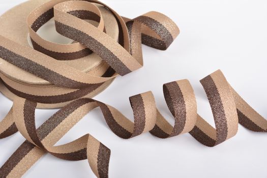 Brown beige Cotton ribbon, roll textilies on bobbin. strapping tape with curl on white backgroud. Use for sewing clothes, bags. Space for text.