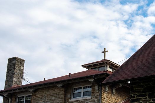 A Cross on the Red Roof of a Cobblestone Convent With a Cloudy Blue Sky Behind It