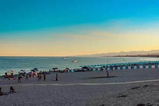 Italian beach with sea and people playing and bathing. Lido on a pebble beach. Blue sky sea