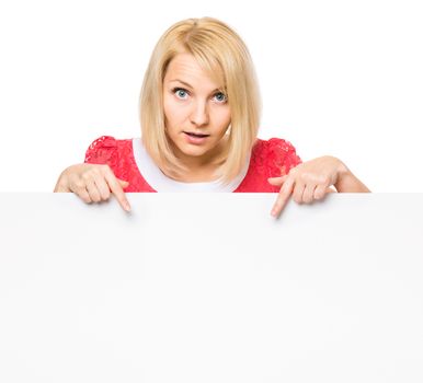 Young woman with surprised eyes peeking out from behind billboard paper poster. Businesswoman holding big white banner, isolated on white background.