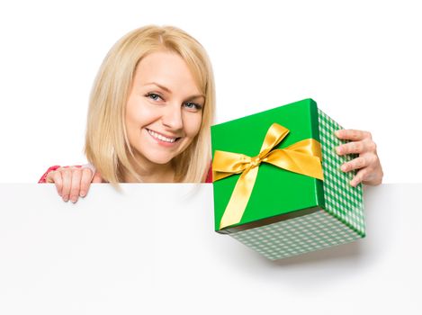 Portrait of happy smiling young woman, showing empty blank signboard with copyspace. Businesswoman holding gift box and peeping behind blank board, isolated on white background.