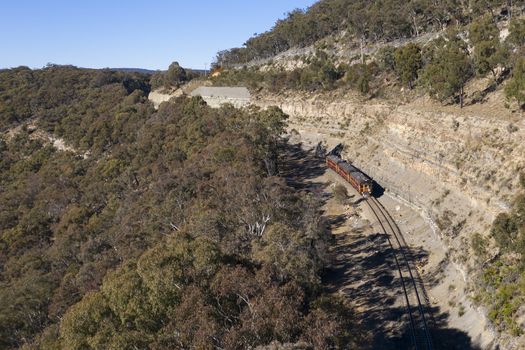 A heritage train running through a valley in rural Australia.