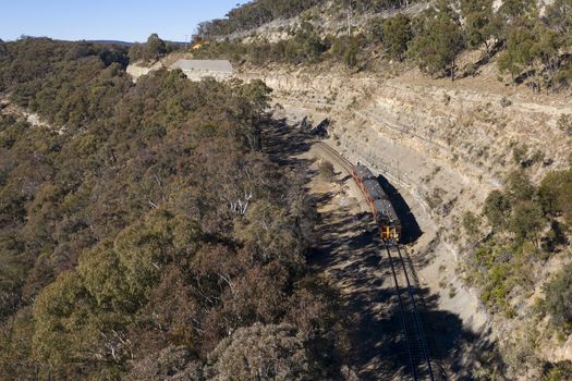A heritage train running through a valley in rural Australia.