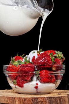 Strawberry and pouring cream on a black studio background