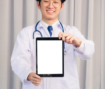 Portrait closeup of Happy Asian young doctor handsome man smiling in uniform and stethoscope neck strap showing front blank screen smart digital tablet on hand, Healthcare medicine concept