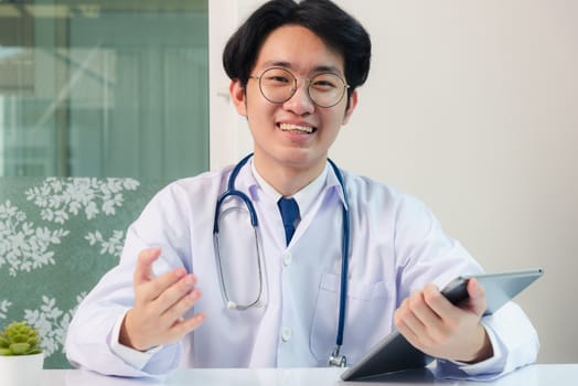 Happy Asian young doctor handsome man smile wear glasses use modern smart digital tablet computer explain patients symptoms of illness on desk at hospital office, Technology Healthcare And Medicine