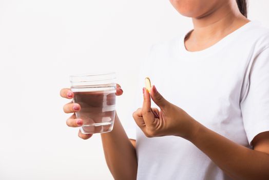 Closeup young Asian woman hold fish oil vitamin drugs in hand ready take medicines with a glass of water, studio shot isolated on white background, Healthcare and medical pharmacy concept