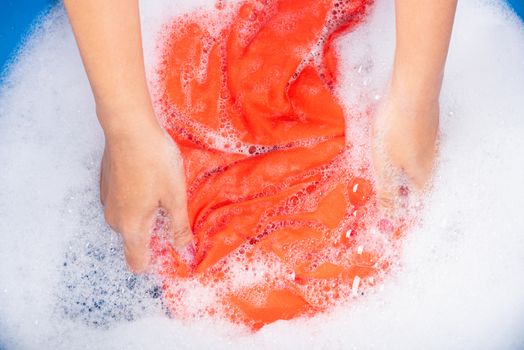 Closeup young Asian woman use hands washing color clothes in basin with detergent have soapy bubble water, studio shot background, laundry concept