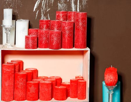 Thick New Year's Christmas candles in white and red are as in a frame, with glass candlesticks, in an old wooden box and on top against a background of a brown board., Space for text.