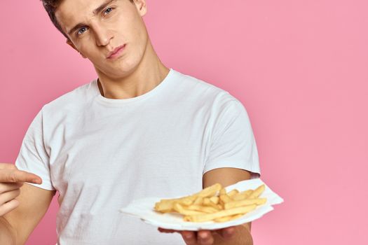 Man with French fries in a paper box on a pink background calories fast food portrait pink background. High quality photo