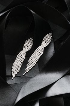 Luxury diamond earrings on black silk ribbon as background, jewelry and fashion brands