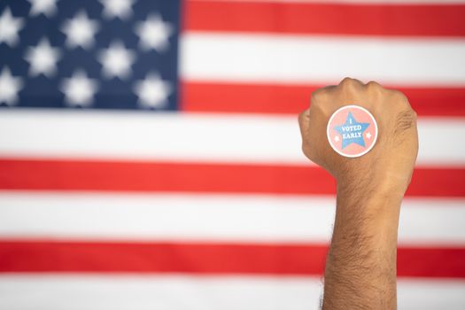 Rising fist with I voted early sticker on hand with US flag as background - Concept of early voting at US election