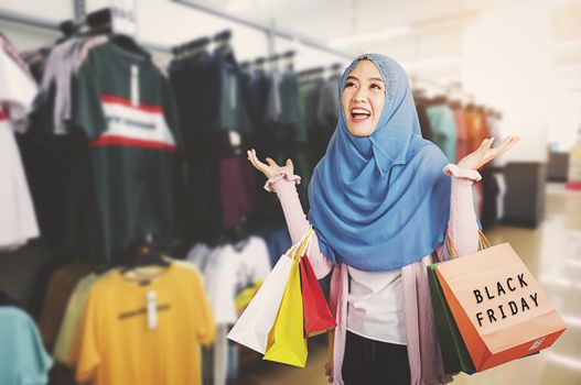 Happy beautiful young woman Muslim smiling funny wear veil hijab she excited holding shopping bags multi color on the mall background with copy space, Black Friday sale concept