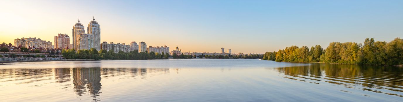 Panoramic view oth the high Obolon buildings near the Dnieper river in Kiev, Ukraine. Blue clear sky and reflection in the water.