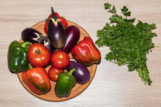 A top close-up shot of various vegetables like tomatoes, parsley, peppers, eggplants lying on a wooden cooking board. Isolated on wooden background.