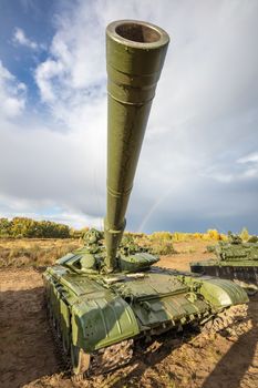 A high angle shot of russian tank T-64 in the field. Cannon pointing upwards straight in the camera. Blue cloudy sky as a background.