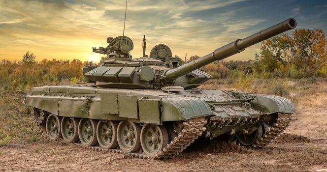 A side shot of russian tank T-64 in the field. Beautiful sunset sky as a background.