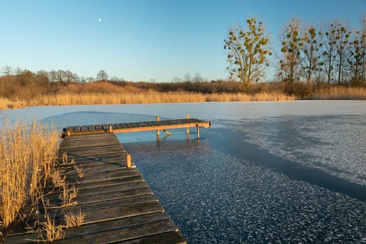 Wooden bridge over the frozen lake and reeds, winter view