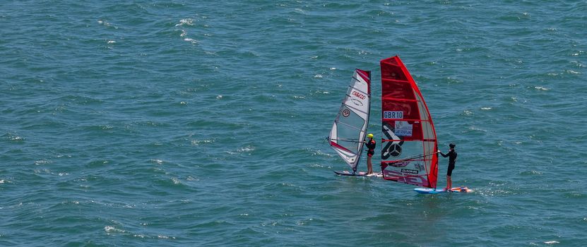 Portland harbour, United Kingdom - July 2, 2020: High Angle aerial panoramic shot of two sail boards with professional surfers on them in Portland harbour.