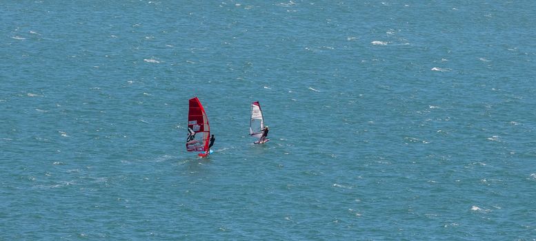 Portland harbour, United Kingdom - July 2, 2020: High Angle aerial panoramic shot of two sail boards with professional surfers on them racing in Portland harbour.