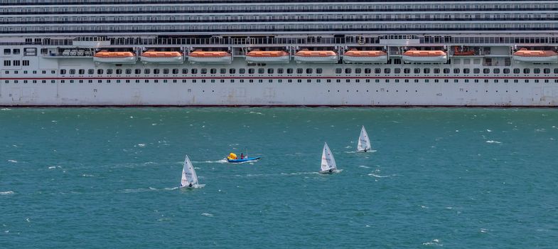 Portland harbour, United Kingdom - July 2, 2020: High Angle aerial panoramic shot of the laser class sailing racing dinghies and a rescue boat sailing by a huge cruise ship in Portland harbour.