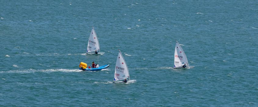 Portland harbour, United Kingdom - July 2, 2020: High Angle aerial panoramic shot of the laser class sailing racing dinghies and a rescue boat in Portland harbour.