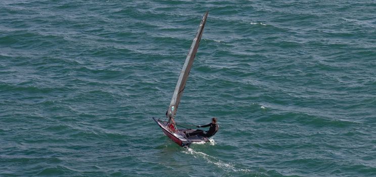 Portland harbour, United Kingdom - July 2, 2020: High Angle aerial panoramic shot of a single racing boat in Portland harbour. Man wearing black swim suit.
