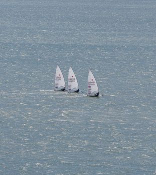 Portland harbour, United Kingdom - July 3, 2020: High Angle aerial portrait format shot of three laser class sailing racing dinghies in Portland harbour.