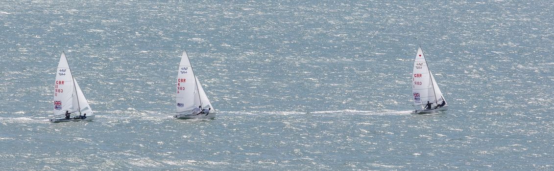 Portland harbour, United Kingdom - July 3, 2020: High Angle aerial panoramic shot of three laser class racing dinghies with one of them sailing way ahead of the first two