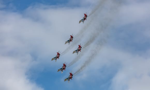 Barnaul, Russia - September 18, 2020: A low angle shot of Strizhi MiG-29 fighter jet squadron performing stunts during an aeroshow. Blue cloudy sky as a background.