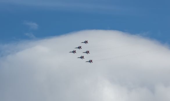 Barnaul, Russia - September 18, 2020: A low angle distant shot of Strizhi MiG-29 fighter jet squadron performing stunts during an aeroshow. Blue cloudy sky as a background.