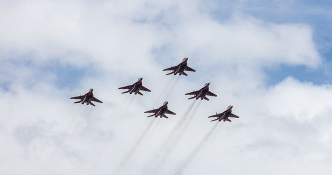 Barnaul, Russia - September 18, 2020: A low angle shot of Strizhi MiG-29 fighter jet squadron performing stunts during an aeroshow. Blue cloudy sky as a background.