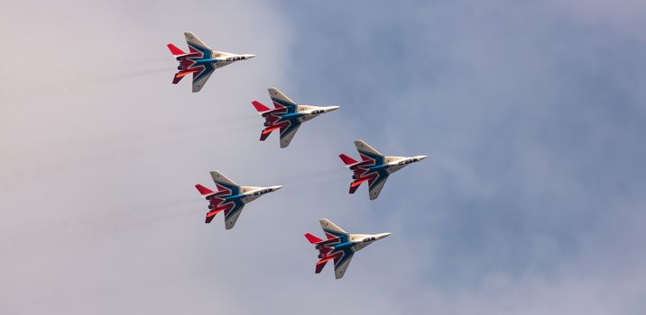 Barnaul, Russia - September 19, 2020: A low angle shot of Strizhi MiG-29 fighter jet squadron performing stunts during an aeroshow. Blue cloudy sky as a background.