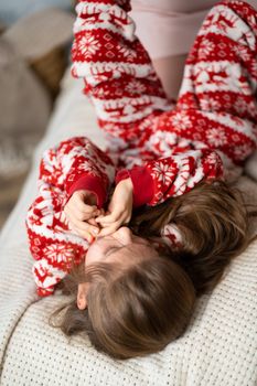 Little girl in red pajamas playing with mom on the bed.