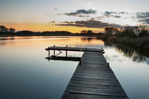 Wooden pier on a calm lake, view after sunset, autumn day