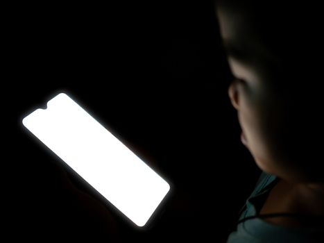 A boy looking at a white blank phone screen on a dark black background.