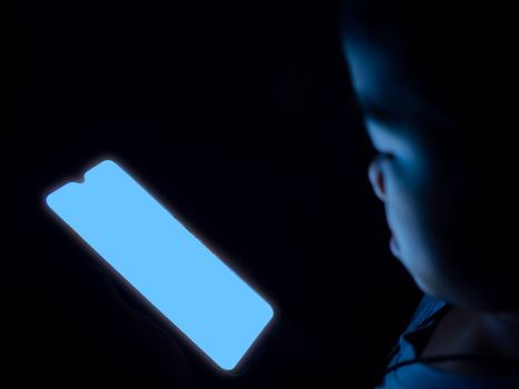 A boy is using a phone with a blank blue screen on a dark black background..