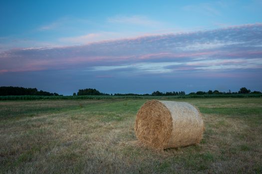 Hay bale in a meadow and colorful clouds on the sky, summer evening view