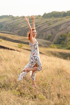 Beautiful red-haired girl is having fun and dancing in a field at sunset.