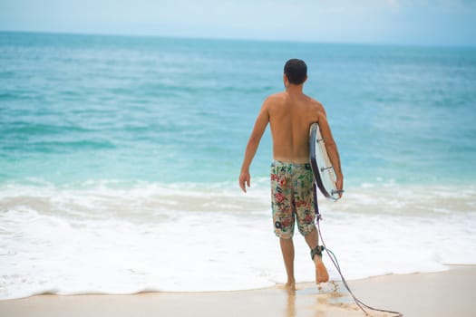 Surfer. Surfing Man With Surfboard Walking On Sandy tropical Beach. Healthy Lifestyle, water activities, Water Sport. Beautiful Ocean