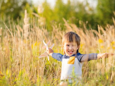 Cute toddler plays with toy airplane on field. Happy kid dreams to be a pilot. Boy is planning for the future. Golden sunset hour at autumn season.